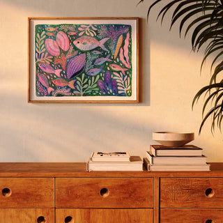 Art Print of an original artwork by Lee Foster-Wilson of fish, shells and seaweed displayed in a wooden frame in a sunlit living room